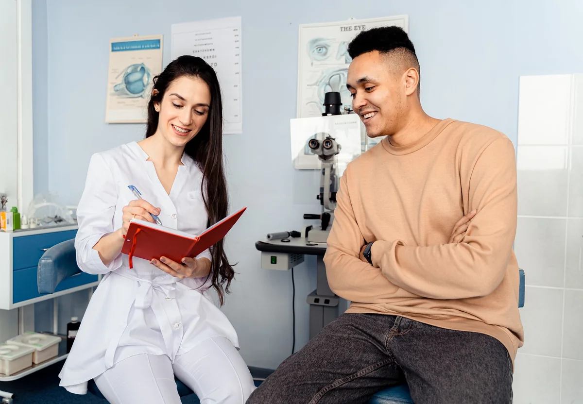 Doctor taking notes while talking with a smiling patient in a clinic
